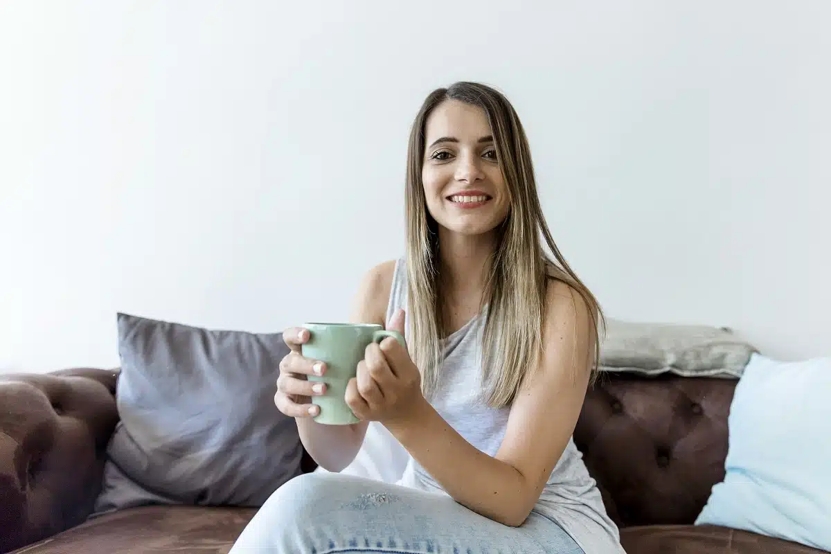 Pessoa sorrindo em casa com uma xícara de café, representando o equilíbrio financeiro e a simplicidade de viver bem gastando menos.